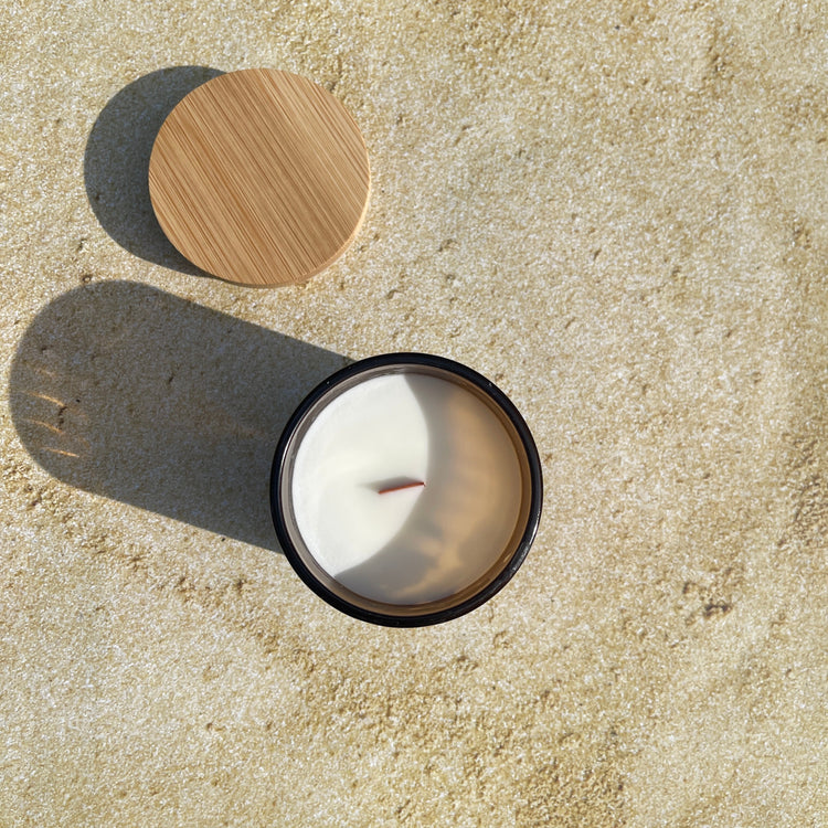 Amber Glass soy candle with bamboo lid on a sandy beach