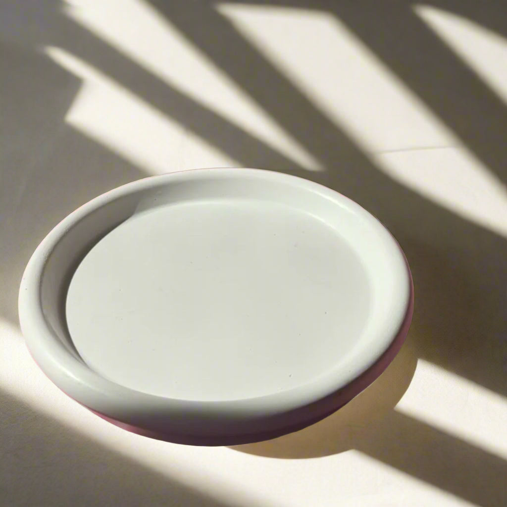 A white concrete candle dish with a minimalist design, displayed in natural lighting casting shadows on its surface.