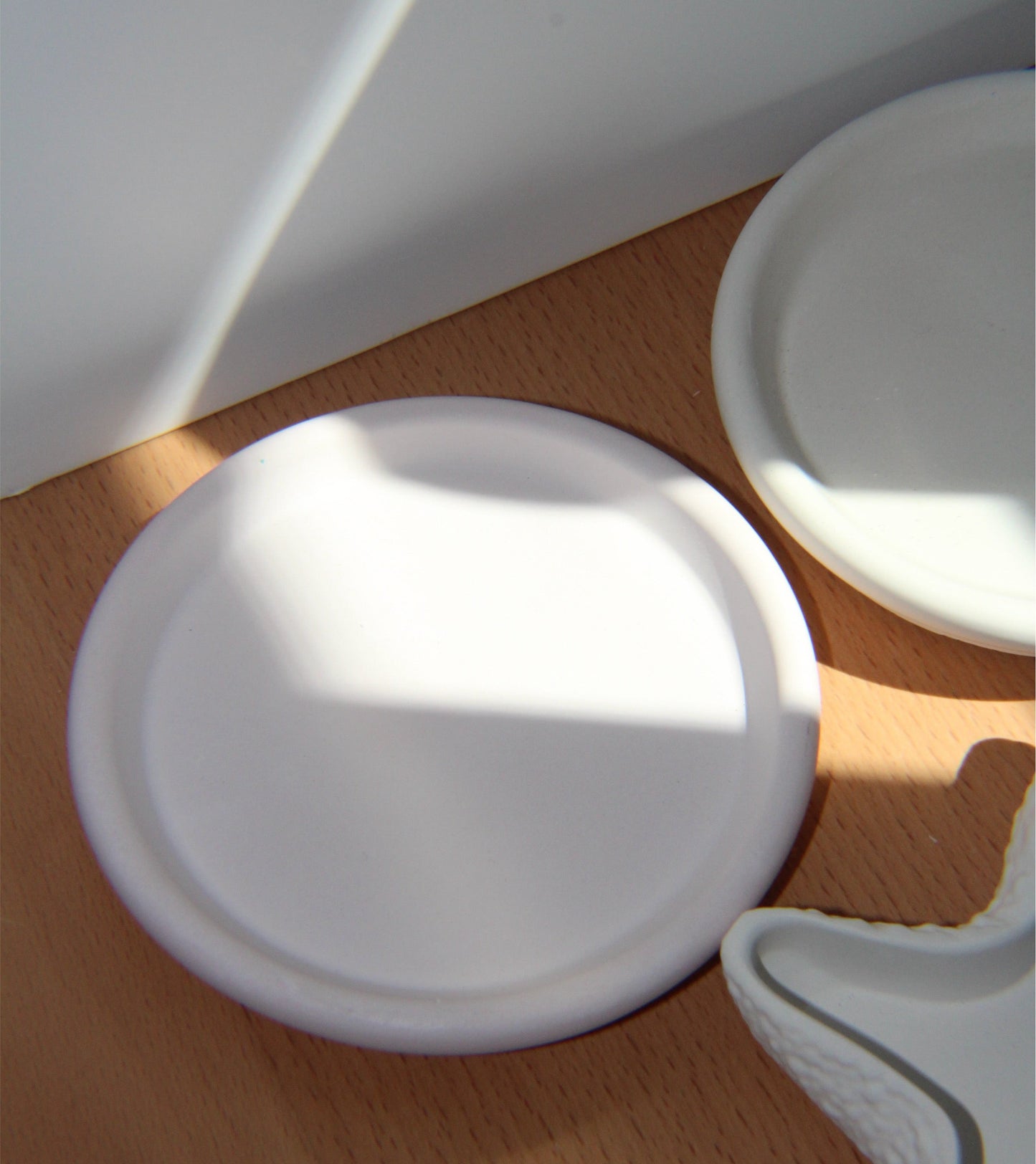 A white porcelain concrete candle dish is displayed on a wooden surface, with a focus on its sleek and minimalistic design.